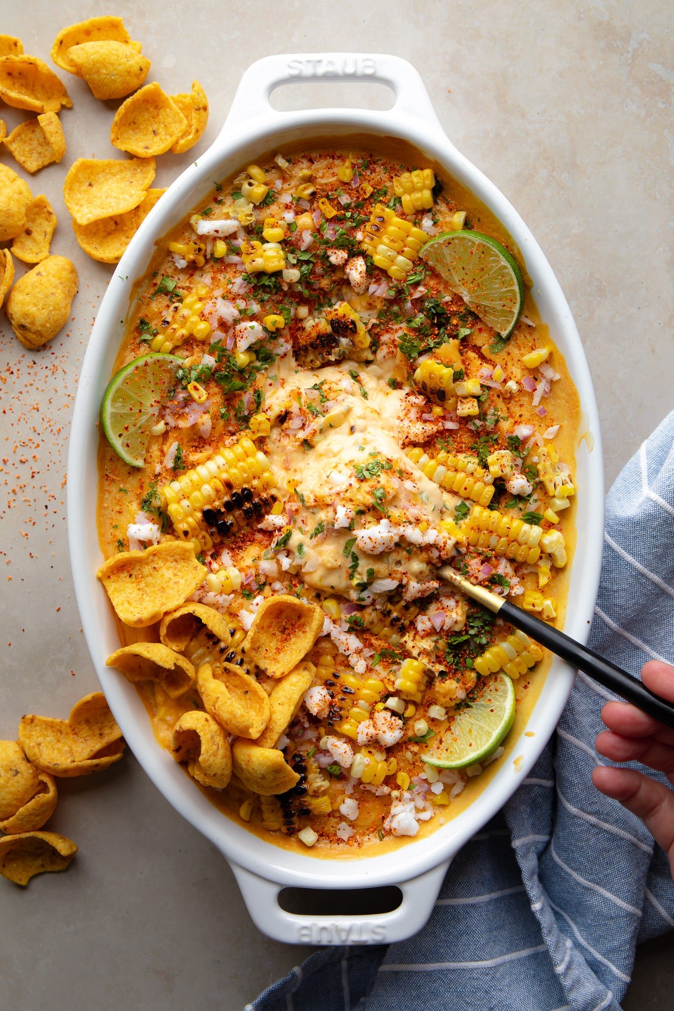 Uma colher preta em um lote de mergulho de milho de rua mexicano vegan em uma assadeira.